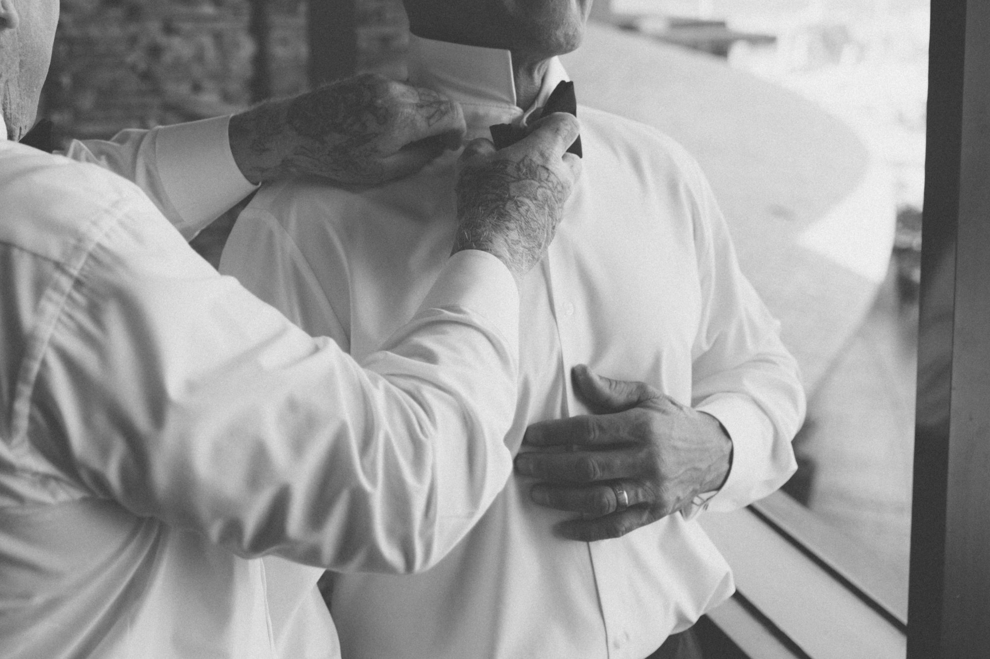 Groom getting ready, friend helping with the bow tie, candid moment captured by Manuel & Alma